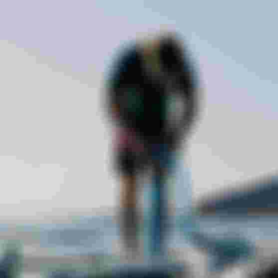 Person inflating a sup on a beach using a pump, with waves and a distant hill in the background.