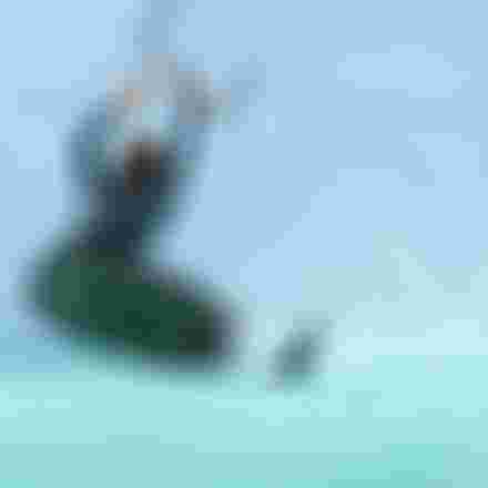 Male kiteboarder performing a dynamic trick on turquoise water, board tilted vertically with water spray, holding kite bar overhead.