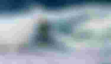 Surfer skillfully rides a large, crashing wave, surrounded by white spray, under a clear blue sky.