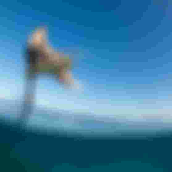 Noe Font kiteboarding on a hydrofoil board over clear blue water.