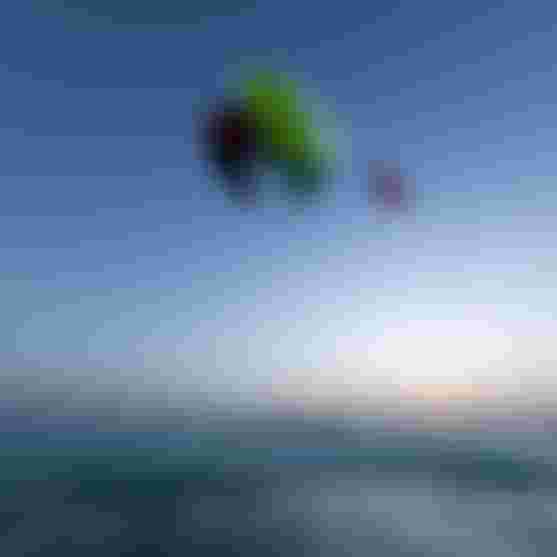 Kitesurfer performing a high aerial trick with a neon green Duotone board over ocean waves at dusk against a blue sky.