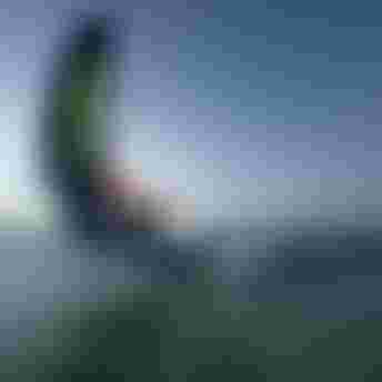 Wing foiler executing a low carving turn on open water, holding a Duotone wing, captured with motion blur at dusk.