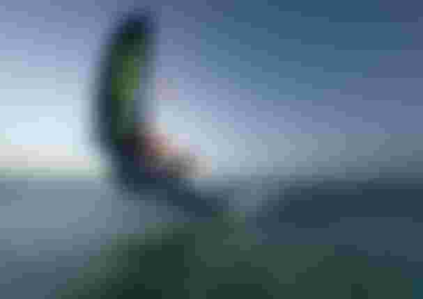 Wing foiler executing a low carving turn on open water, holding a Duotone wing, captured with motion blur at dusk.