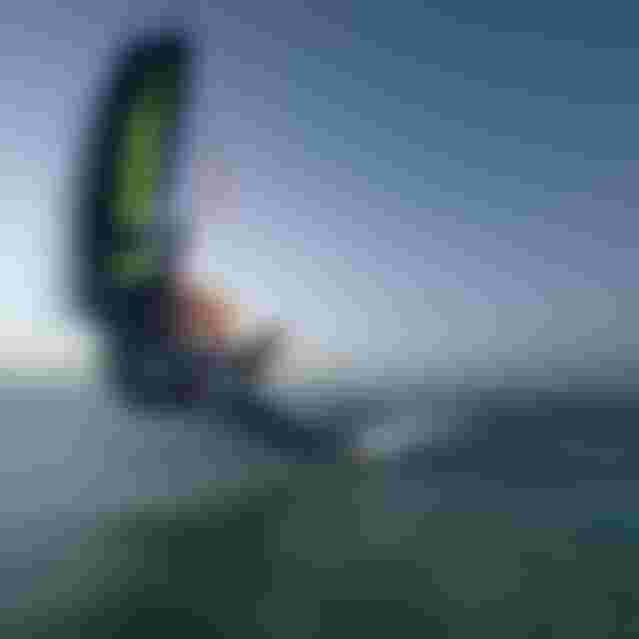 Wing foiler executing a low carving turn on open water, holding a Duotone wing, captured with motion blur at dusk.