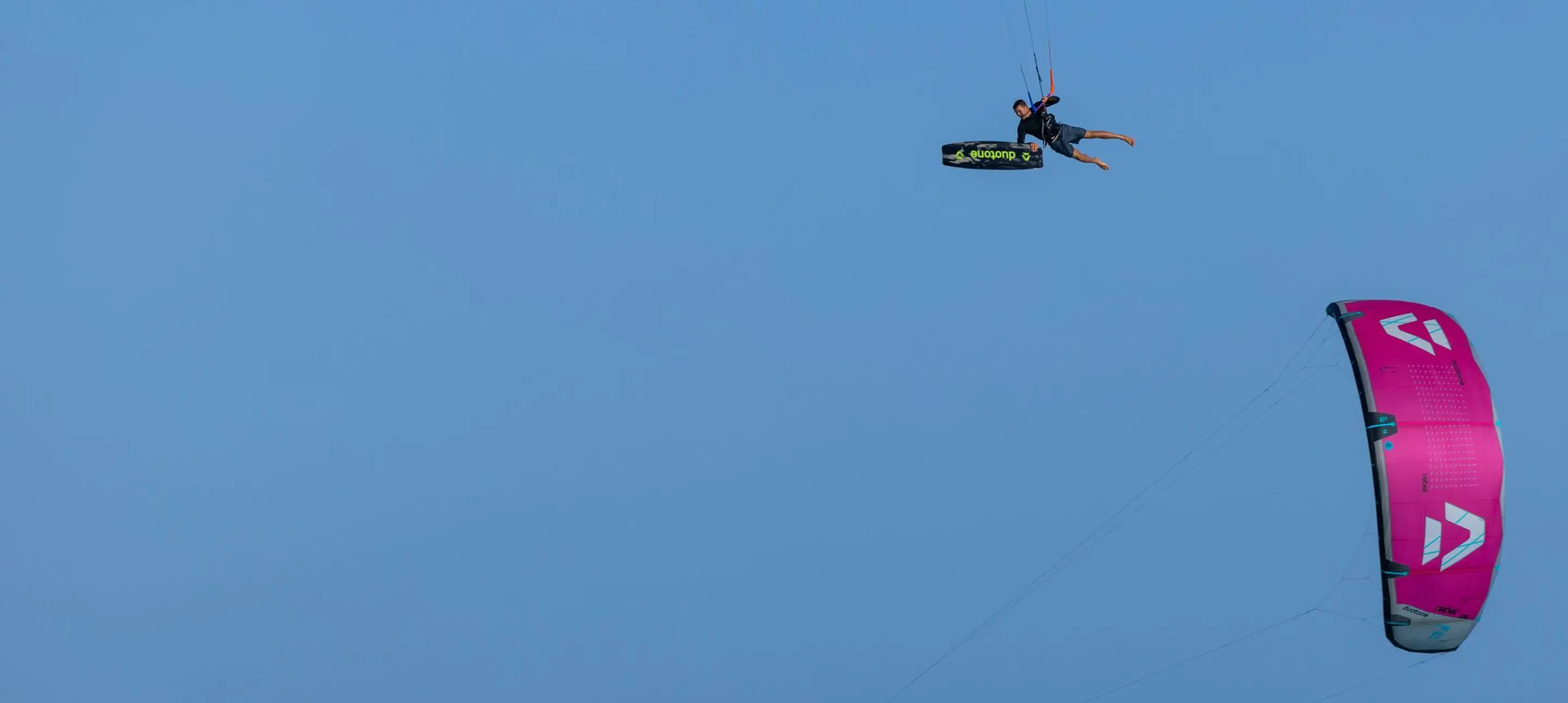 Kitesurfer jumping with a Duotone twintip and pink kite against a blue sky