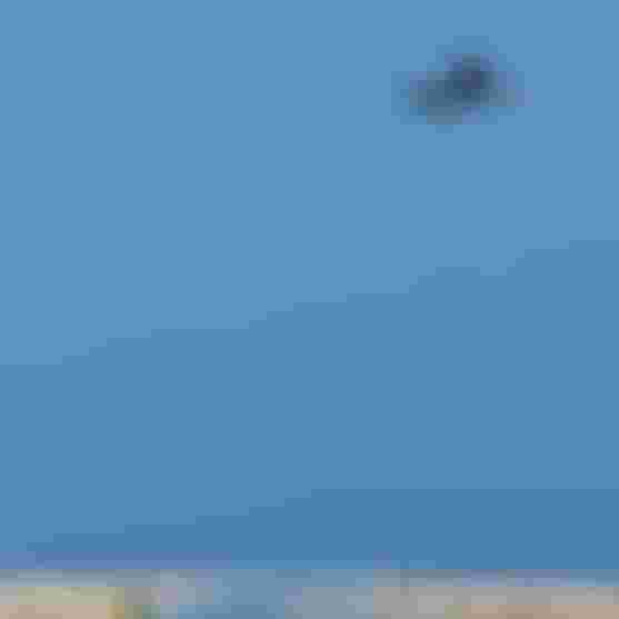 Kitesurfer performing a high aerial trick with a Duotone board, soaring above a beach under a clear blue sky with a pink kite.