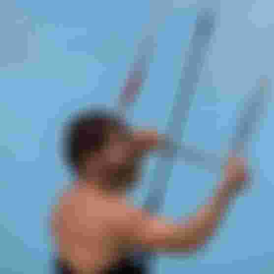 Male kitesurfer gripping a control bar with both hands against a clear blue sky, focused and ready to ride.