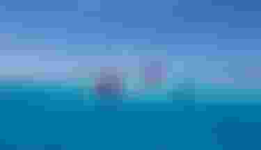Five colorful kitesurfers riding across vivid turquoise water under a clear blue sky in a tropical lagoon setting.