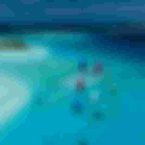 Aerial view of kitesurfers with colorful kites gliding over a crystal-clear turquoise tropical lagoon near a sandy sandbar.