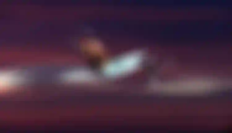 A shirtless man kitesurfing mid-air with a hydrofoil board against a dramatic dark red and purple sunset sky.