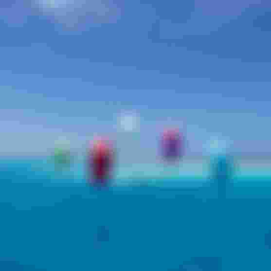 Multiple kitesurfers riding colorful kites over vivid turquoise tropical waters under a clear blue sky