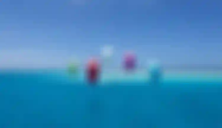 Multiple kitesurfers riding colorful kites over vivid turquoise tropical waters under a clear blue sky