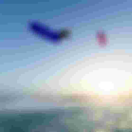 Kitesurfer performing a high aerial trick with a blue Duotone board and pink kite over turquoise ocean at sunset.