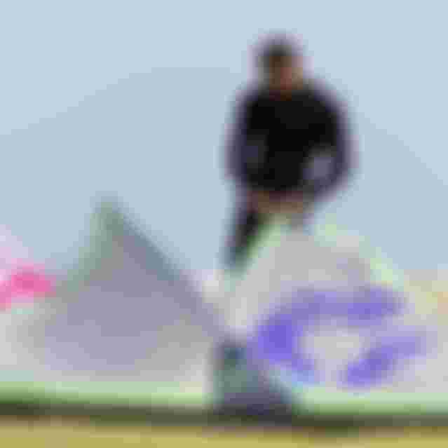 Man in black wetsuit preparing Duotone kitesurfing kites on a grassy beach area, adjusting lines before a session.