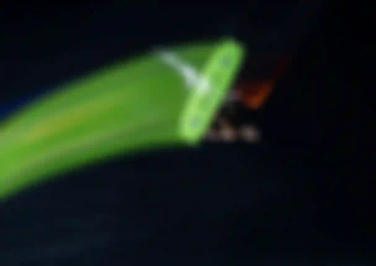 Aerial night shot of a kitesurfer gripping a neon green Duotone board mid-trick over dark water with motion blur trails.