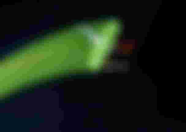 Aerial night shot of a kitesurfer gripping a neon green Duotone board mid-trick over dark water with motion blur trails.