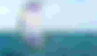 Kitesurfer riding a hydrofoil board on turquoise water with a large Duotone Rebel kite in white, purple, and green.