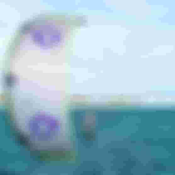 Kitesurfer riding a hydrofoil board on turquoise water with a large Duotone Rebel kite in white, purple, and green.