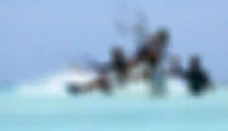 Group of kitesurfers riding through shallow turquoise water on a sunny day, with kite lines and colorful bars visible above.