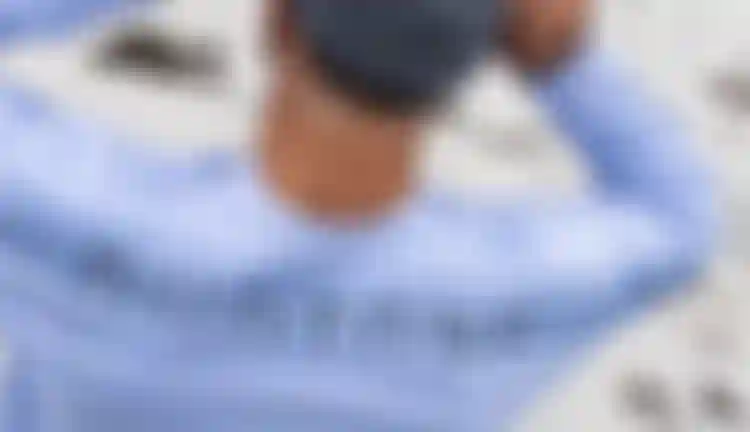Rear view of a rider wearing a light blue Duotone long-sleeve shirt and grey beanie on a sandy beach.