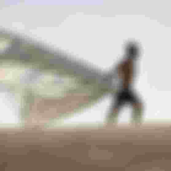 Reno Romeu walking on sand, carrying a kite Evo under a clear sky.