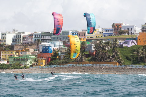 Duotone Vegas LEI kite durante kitesurf en una colorida ciudad costera con edificios en la ladera