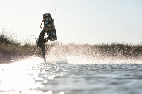 Tabla de kitesurf twin-tip Duotone Team Series durante el kitesurf en un spot de agua plana con dunas cubiertas de hierba