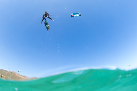 Tavola da kitesurf Duotone Select Textreme twin-tip durante il kitesurf sull'oceano con colline
