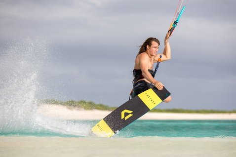 Duotone Select Textreme twin-tip kiteboard durante il kitesurf su una spiaggia tropicale con acque turchesi basse