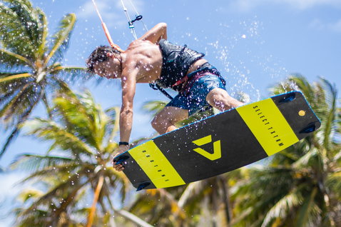 Duotone Select Textreme twin-tip kiteboard durante il kitesurf su una spiaggia tropicale con palme