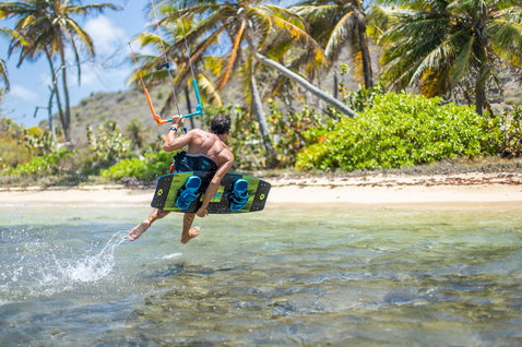 Duotone Select Textreme twin-tip kiteboard durante il kitesurf in una laguna tropicale con palme