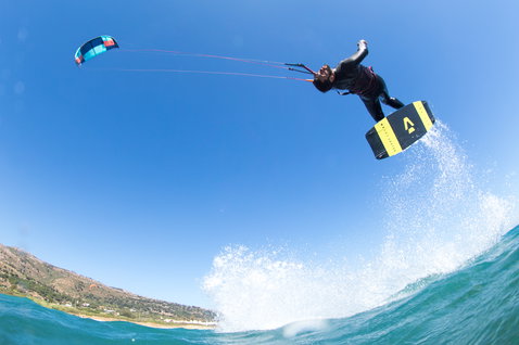 Duotone Select Textreme twin-tip kiteboard durante il kitesurf su spiaggia oceanica con colline costiere