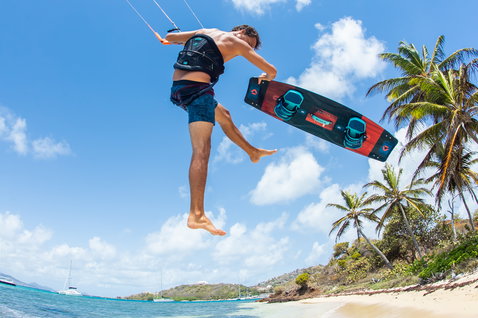 Duotone Select twin-tip kiteboard durante il kitesurf su una spiaggia tropicale con palme