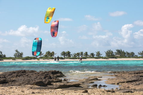 Duotone Neo LEI kite during kitesurfing over a tropical beach lagoon with rocky foreground and palm trees