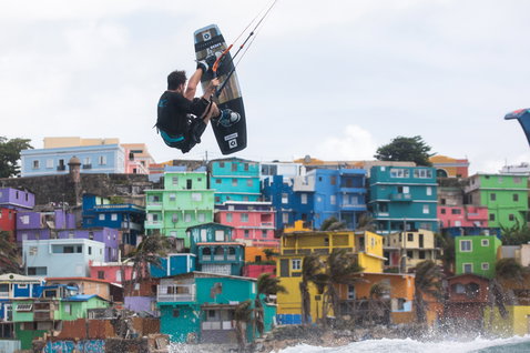 Duotone Team Series TS tabla de kitesurf twin-tip durante el kitesurf en una zona costera urbana colorida