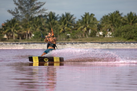 Duotone Select Textreme twin-tip kiteboard durante il kitesurf in una laguna tropicale con palme