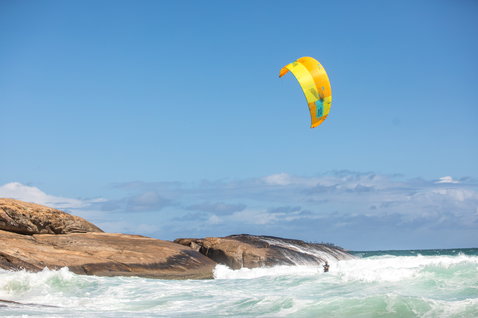 Duotone Evo LEI kite during kitesurfing on a rocky ocean coastline with breaking waves