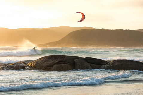 Duotone Neo LEI kite during wave riding at the ocean beach with rocky foreground and mountain backdrop