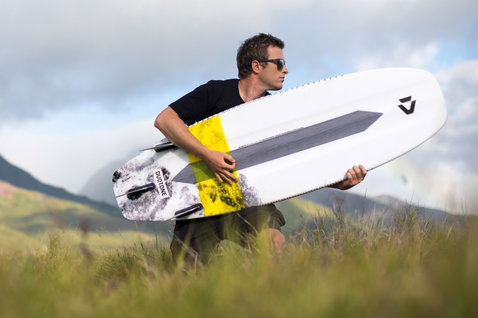 Duotone Pro Whip CSC tabla de kitesurf de olas en pose de pie en ladera de montaña verde