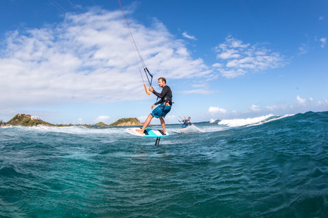 Duotone Spirit Surf 1250/75 Foil Front Wing beim Foilen am tropischen Ozeanstrand mit Inseln im Hintergrund