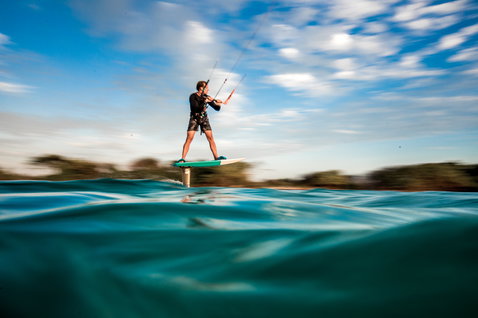 Kite foilboard lors du foiling dans un lagon océanique avec végétation tropicale en arrière-plan