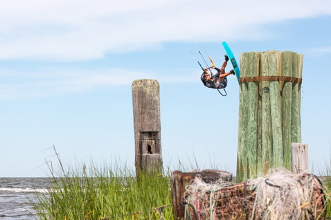 Duotone Click Bar Quad Control bar during kitesurfing at a coastal shoreline with wooden dock pilings and tall grass