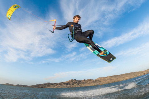 Duotone Entity Ergo tabla de kitesurf twin-tip durante kitesurf en laguna costera con colinas áridas