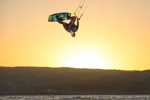Duotone Entity Ergo tabla de kitesurf twin-tip haciendo kitesurf en playa con colinas áridas