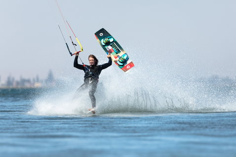 Duotone Entity Ergo tabla de kite twin-tip practicando kitesurf en laguna de aguas planas con horizonte urbano