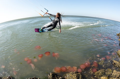 Duotone Entity Ergo twin-tip kiteboard durante el kitesurf en una costa oceánica con rocas y medusas bajo el agua