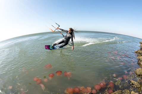 Duotone Soleil Textreme twin-tip kiteboard during kitesurfing in coastal shallow water with rocky shore