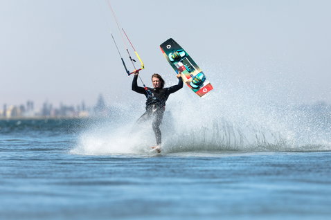 Duotone Jaime Twin-Tip Kiteboard beim Kitesurfen auf einer flachen Wasserlagune mit Stadtsilhouette