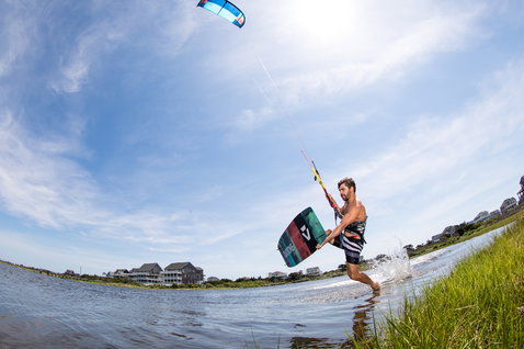 Duotone Spike Textreme twin-tip kiteboard durante il kitesurf in una laguna costiera con case sulla spiaggia