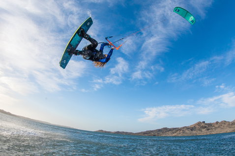 Tavola da kitesurf wake-style Duotone Gambler durante il kitesurf sulla costa oceanica con colline aride